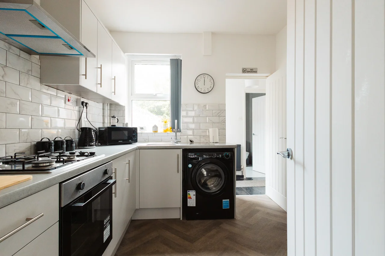 Widnes kitchen with white cabinetry, oven and washing machine beneath the window